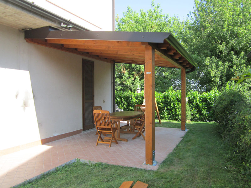 Pergola addossata alla casa con struttura in legno, copertura e pilastri su supporti metallici.